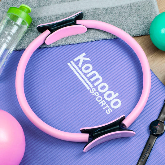 Pink and black resistance band laid on a purple Komodo Sports mat, with a towel, water bottle, exercise ball, and smartwatch nearby.