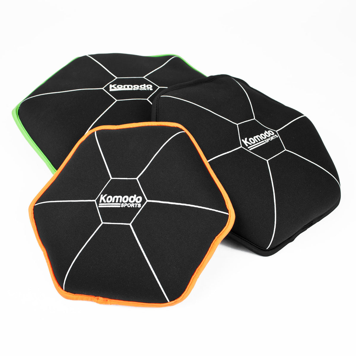 Three Komodo Sports hexagonal sandbags on a white background, featuring black fabric with white lines and colored borders in green, orange, and white.