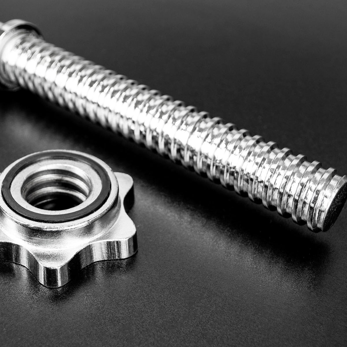 A close-up of a metallic barbell and a matching star-shaped spinlocks on a dark reflective surface.