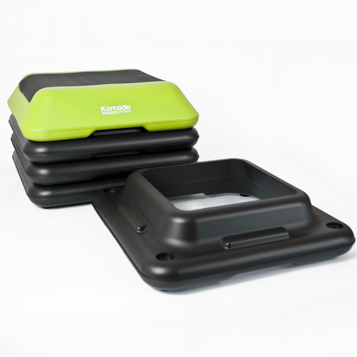 A stack of black step platforms with a bright lime green top step featuring the white 'Komodo Fitness' logo, displayed on a clean white background.