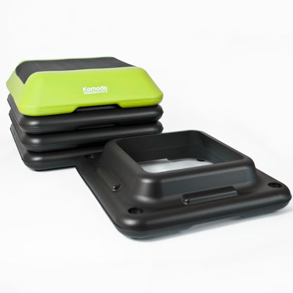 A stack of black step platforms with a bright lime green top step featuring the white 'Komodo Fitness' logo, displayed on a clean white background.