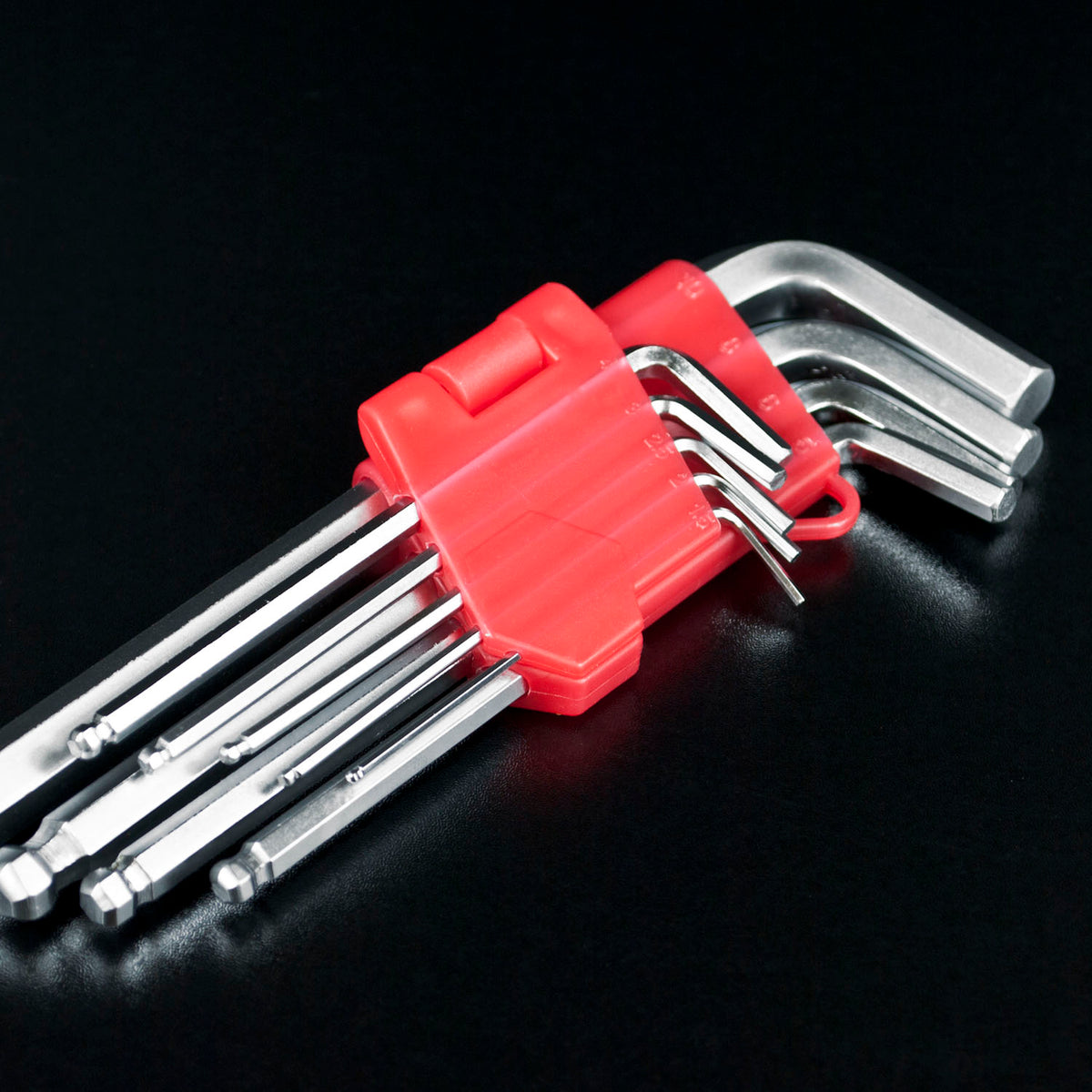 A set of silver hex wrenches with a bright red plastic holder, photographed on a glossy black background.