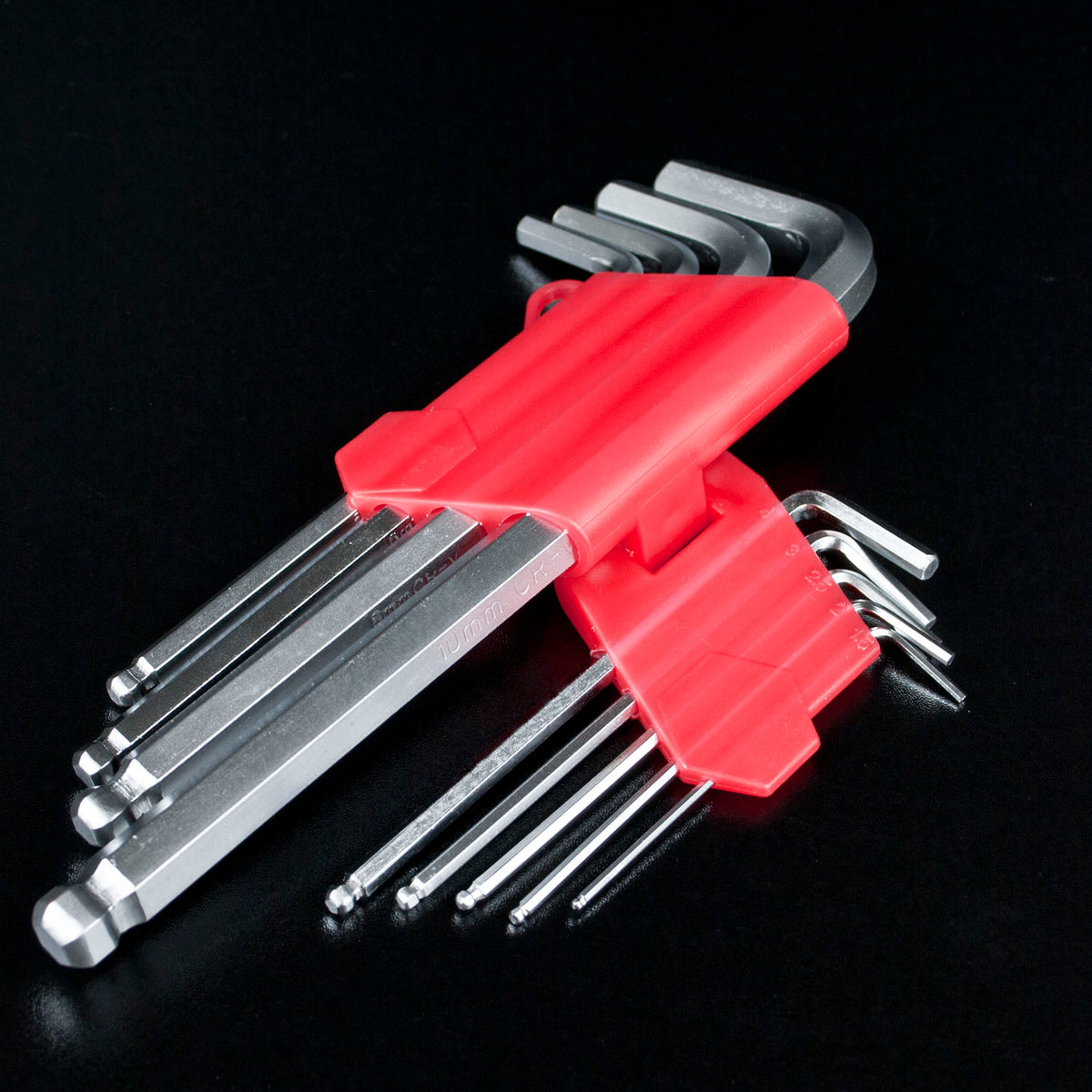 A set of silver hex wrenches with a bright red plastic holder, photographed on a black reflective background.