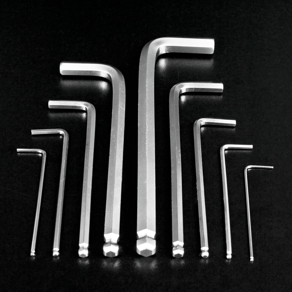 Nine silver metal hex wrenches in different sizes arranged in a symmetrical pattern on a black reflective background.
