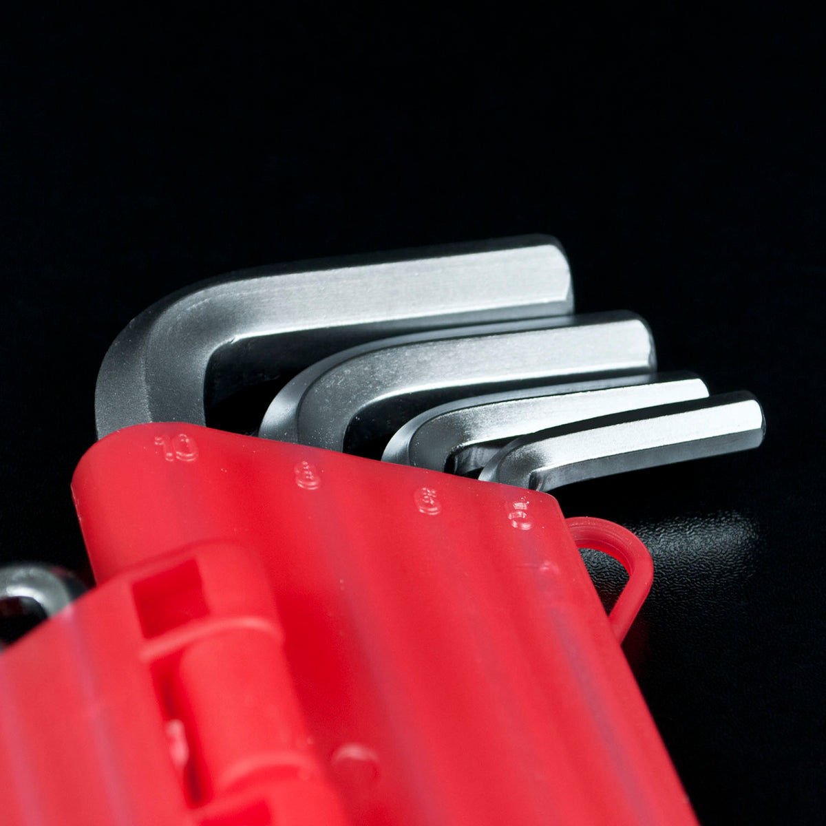 A close-up of a red hex key holder containing several silver metal hex keys, set against a solid black background.