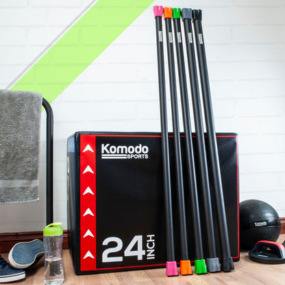 Komodo Sports weight bars. standing upright next to a Komodo Plyo box, on a wooden floor, with a towel, water bottle, and exercise ball in the background.