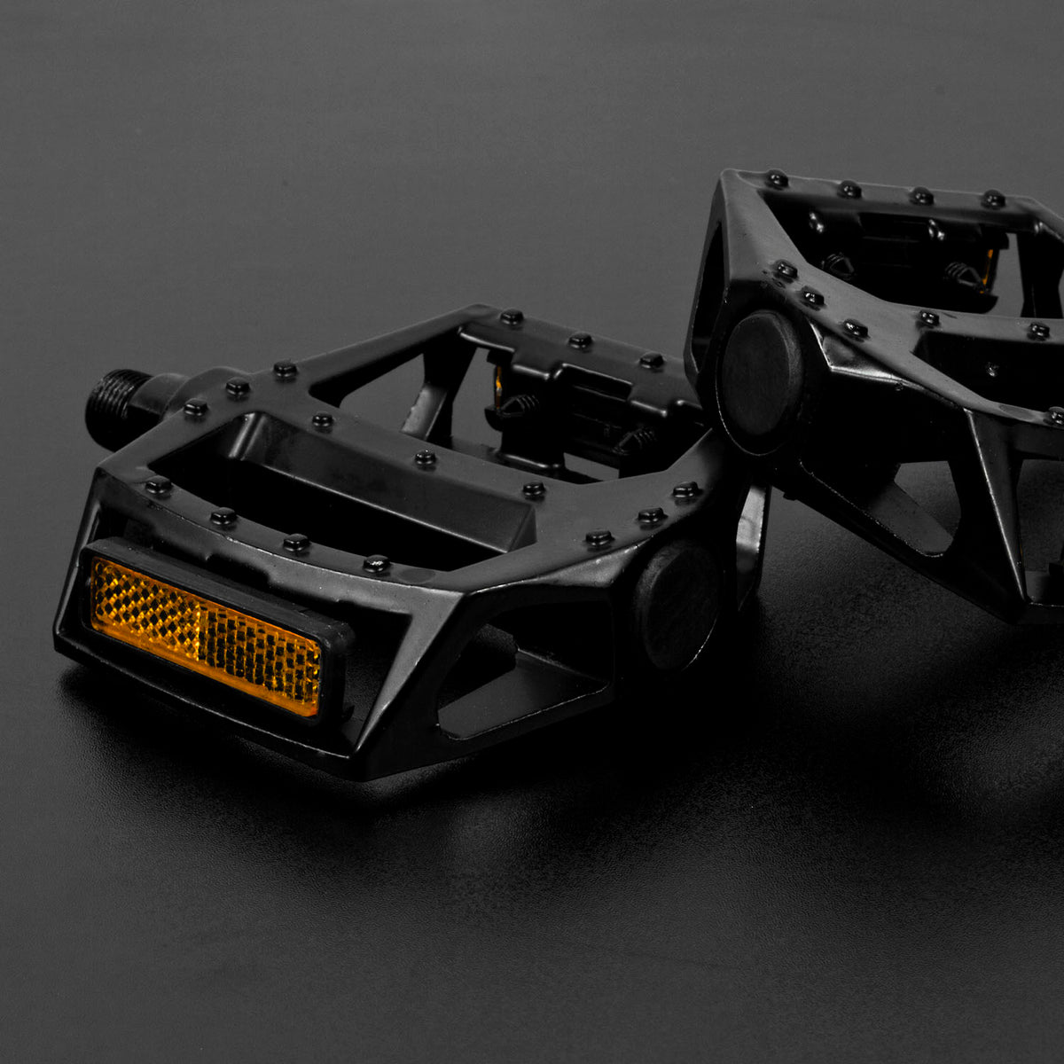 Two black geometric bicycle pedals with a reflective amber light bar, photographed on a dark gray studio background.