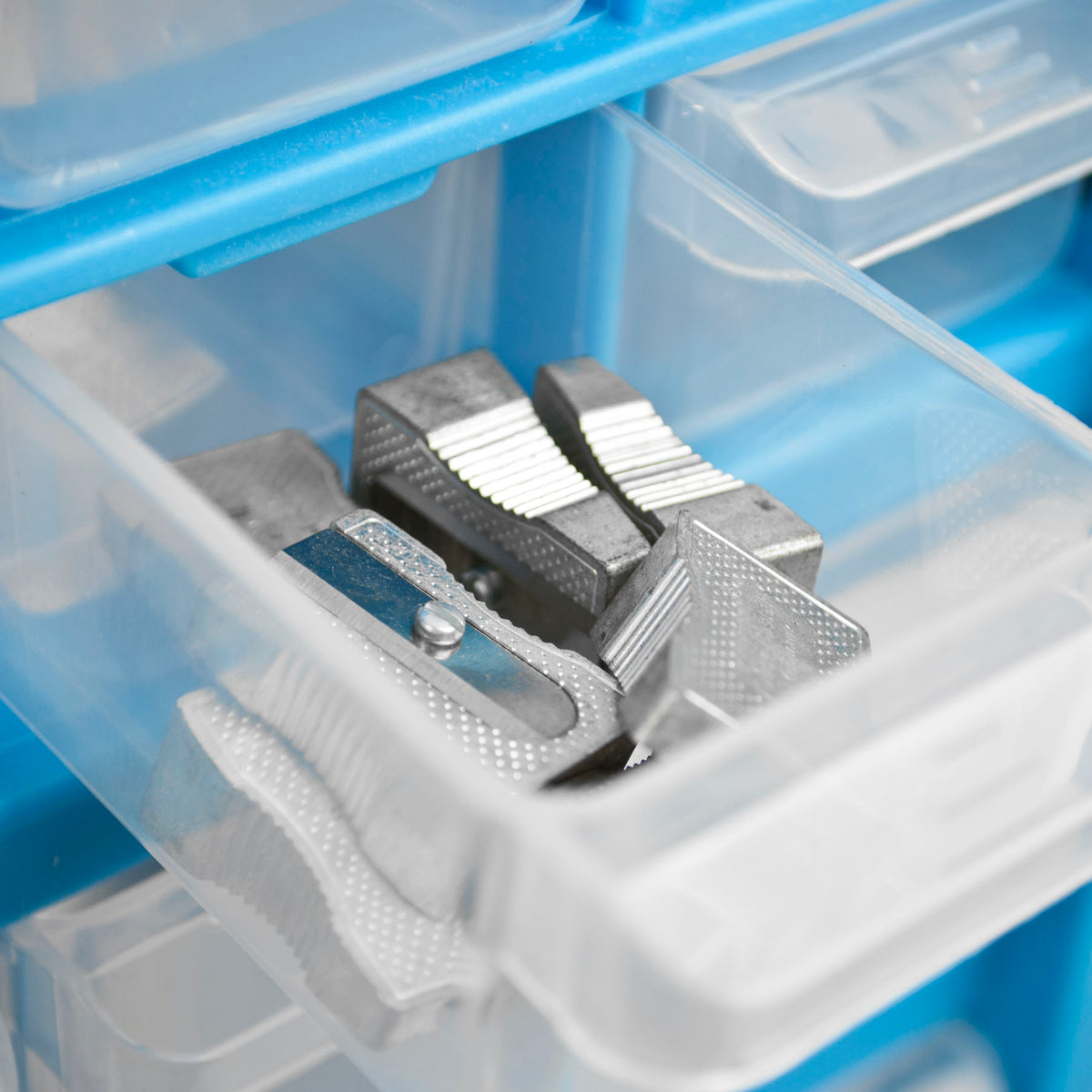 A close-up of a clear plastic organizer drawer containing several small silver metal tools or clips, with a blue drawer frame visible around it.