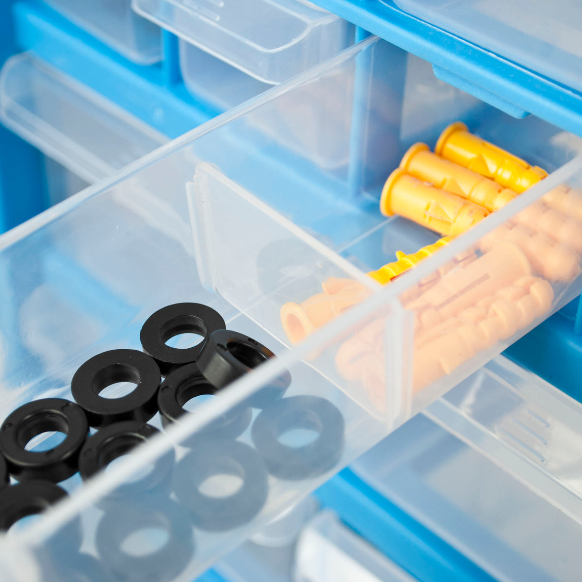 Clear plastic drawer organizer bins inside a blue storage case, holding black rubber grommets and orange plastic wall plugs.