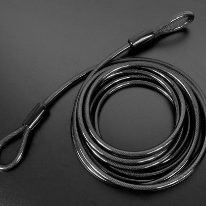 A coiled black steel cable with two looped ends and small connector sleeves, photographed on a dark gray background.