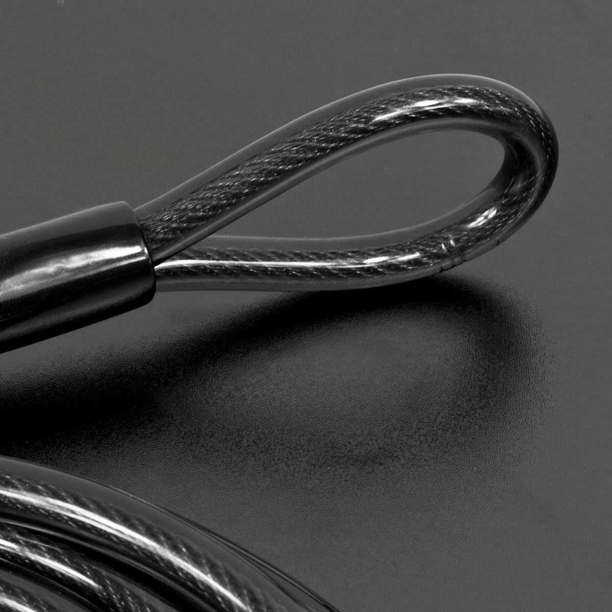 Close-up of a black steel cable loop with a braided wire core and a black sleeve, resting on a dark gray surface.