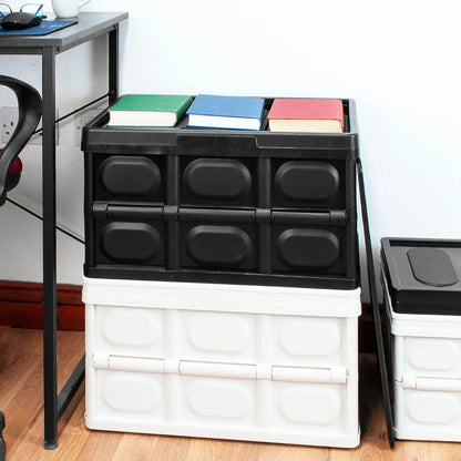 A stackable plastic storage bin set in a home office environment, featuring a black bin on top of a white bin, with three colored books placed on the black bin. A second bin is partially visible on the right.