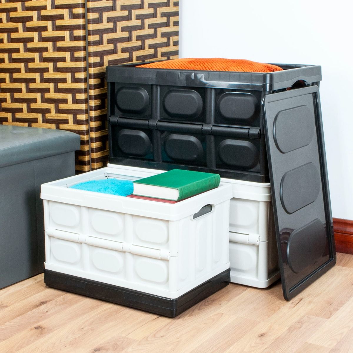 A set of plastic folding storage bins in white and black, shown stacked and open on a wooden floor in a room setting.