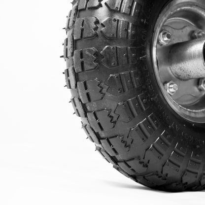 Close-up of a black off-road tire with deep tread blocks and a silver metal wheel hub, photographed on a clean white background.
