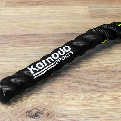A close-up of a black Komodo Sports battle rope handle wrapped in protective foam, resting on a light brown wooden surface.