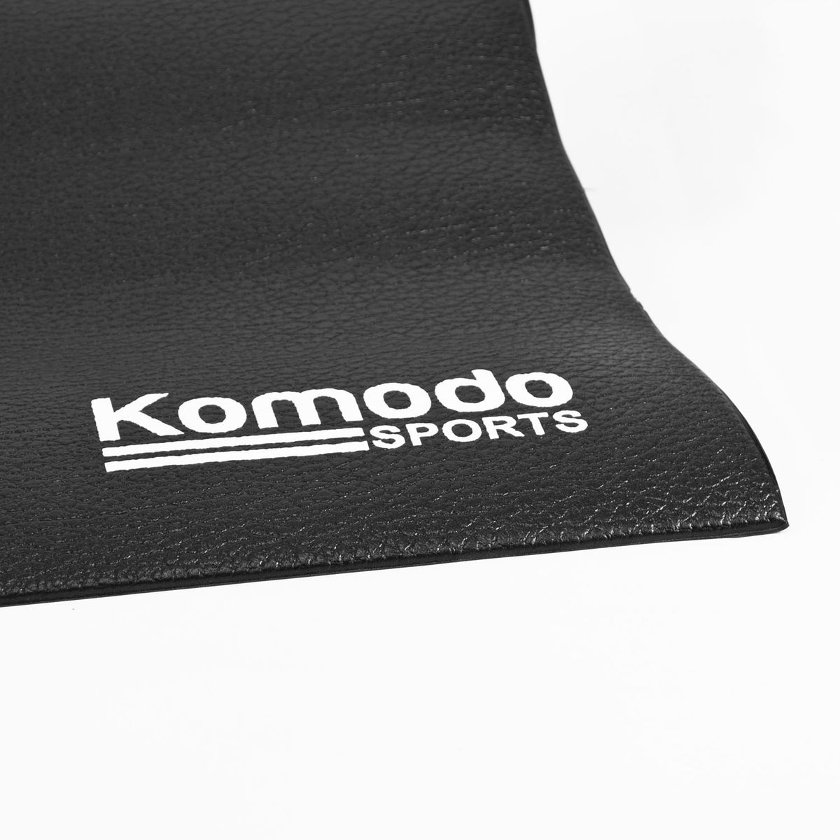 A close-up of a black textured mat with the white 'Komodo Sports' logo printed on it, set against a clean white background.