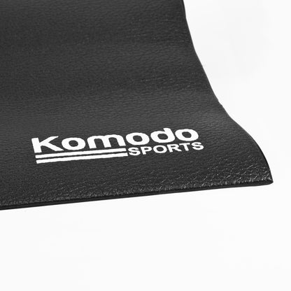 A close-up of a black textured mat with the white 'Komodo Sports' logo printed on it, set against a clean white background.