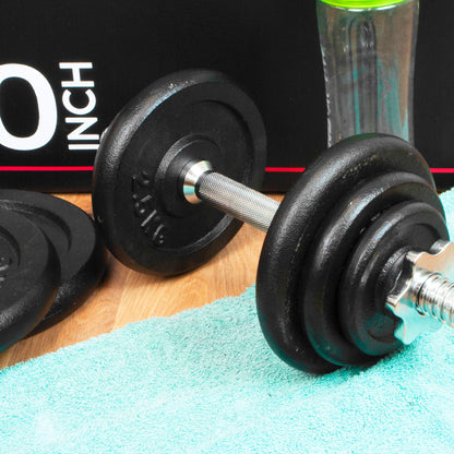 A close-up of a black adjustable dumbbell with a silver metal handle resting on a mint green towel, with a black box and a clear bottle in the background.