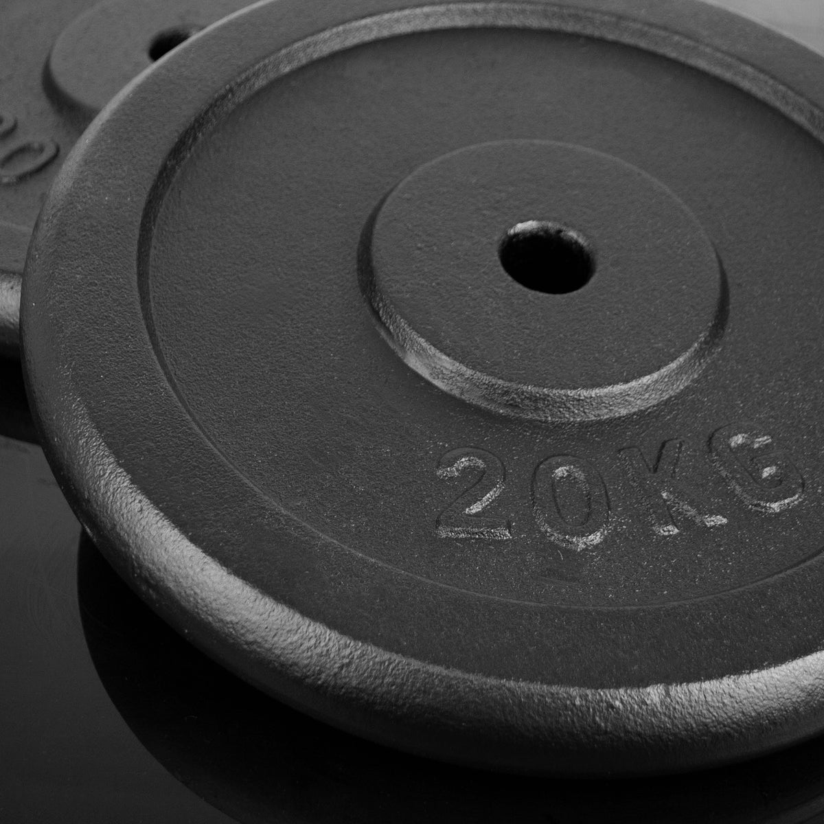 Close-up of a black cast iron weight plate stamped with '20KG' on a dark reflective surface.