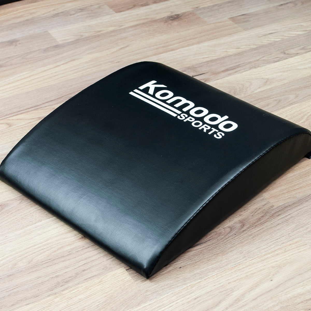 Black Sit Up Ab Pad with 'Komodo Sports' logo on a wooden floor