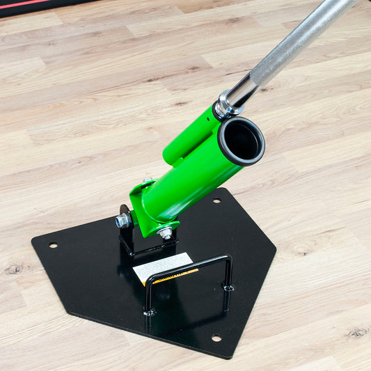A green and black landmine platform with a long barbell, mounted on a black base plate, photographed on a light wood floor.