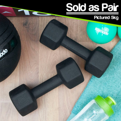 Two black hex dumbbells on a light wood floor, with a black slam ball partially visible on the left, a teal foam ball with the brand name Komodo on the right, a teal towel, and a clear bottle with a green cap. A black banner at the top reads 'Sold as Pair' and 'Pictured: 5kg'.