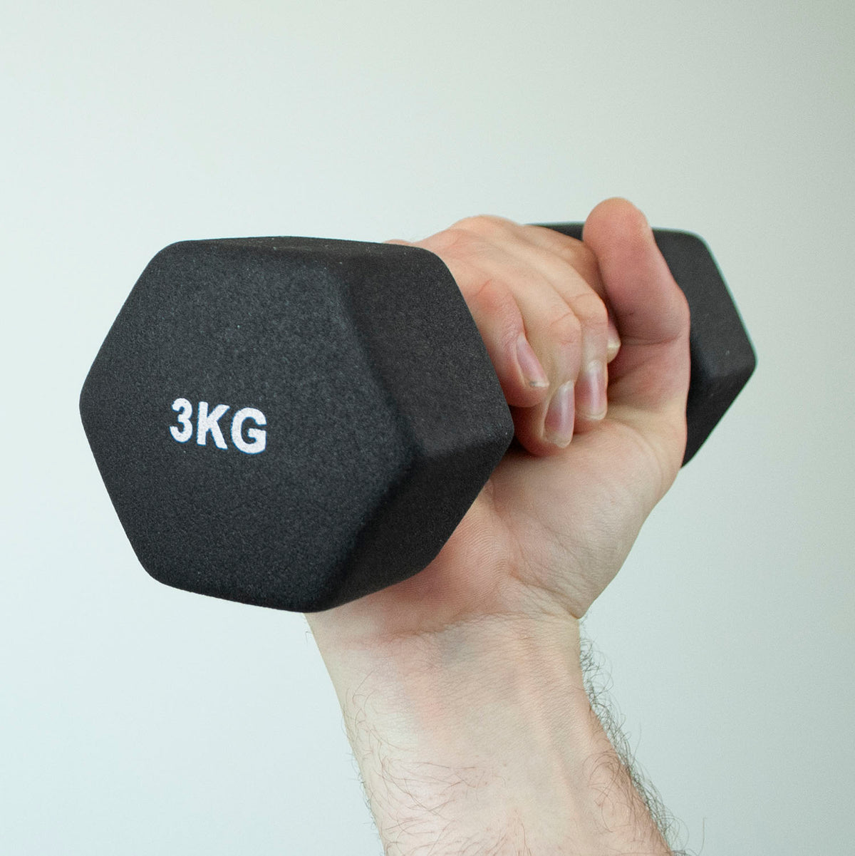 A hand holding a black hexagonal 3KG dumbbell against a plain light gray background.