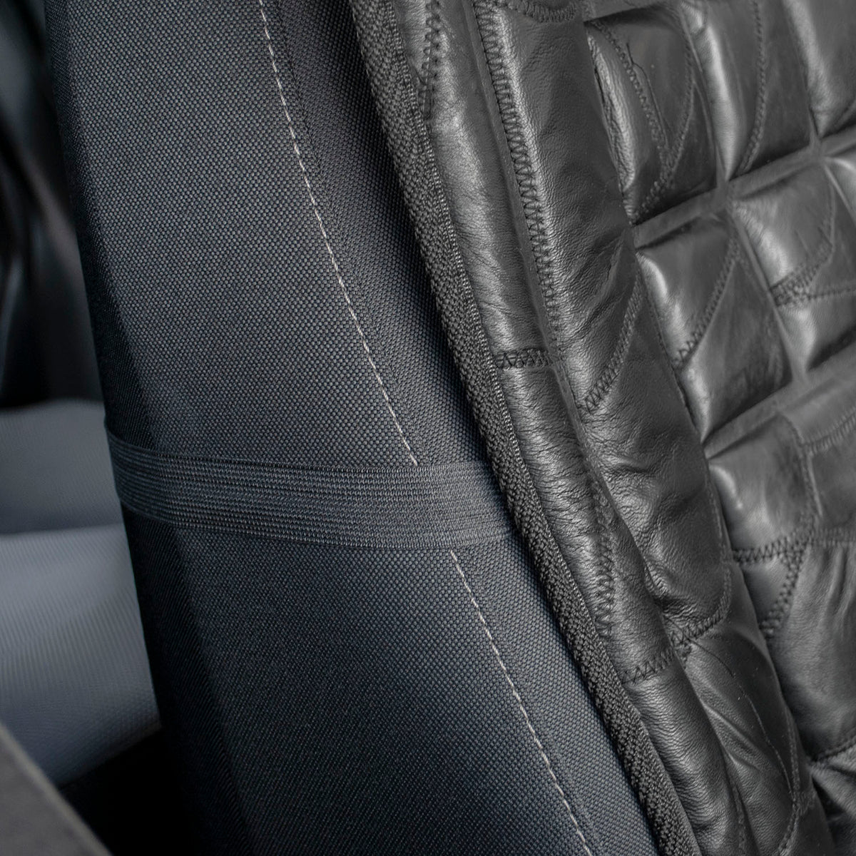 Close-up of a black car seat cover with a quilted diamond pattern on the backrest and a smooth fabric side panel with contrast stitching and a seat belt loop.