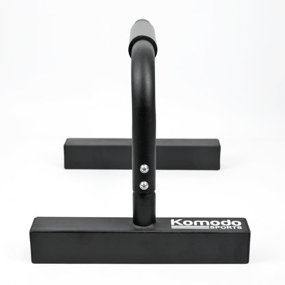 Black metal push-up bar with a wide rectangular base and a curved vertical bar, shown on a clean white background. The brand name 'Komodo Sports' is printed in white on the front of the base.