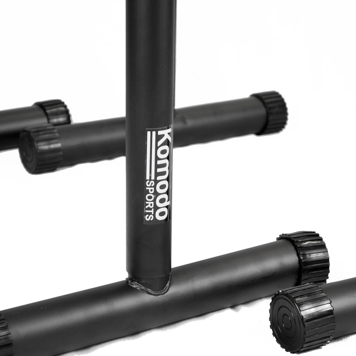 Close-up of a black metal gym stand with the brand name 'Komodo Sports' printed vertically in white on the center post, set against a clean white background.