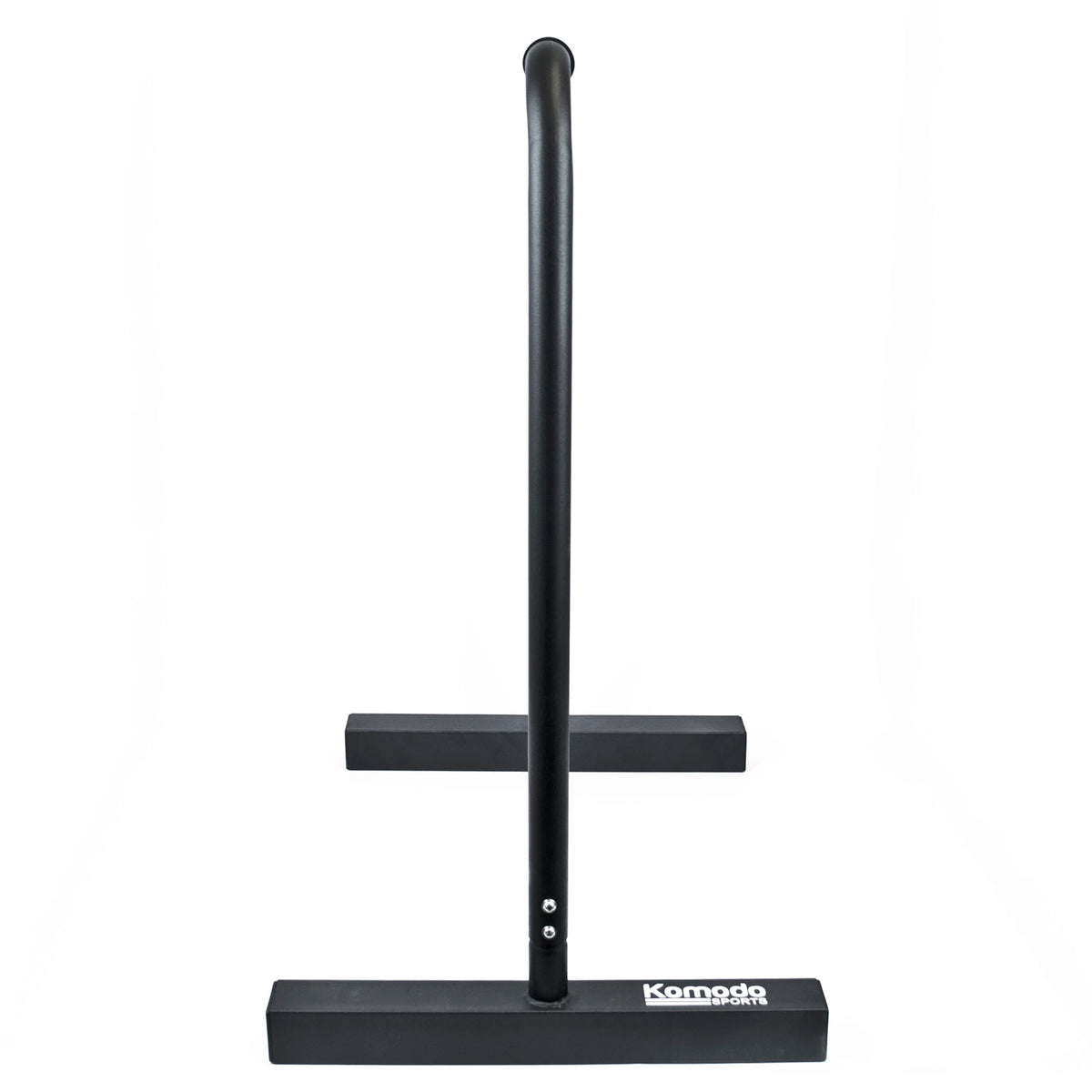 A black metal dip bar with a wide rectangular base and a vertical upright, shown on a plain white background. The brand name 'Komodo' is printed in white on the front of the base.