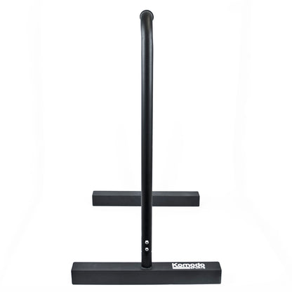 A black metal dip bar with a wide rectangular base and a vertical upright, shown on a plain white background. The brand name 'Komodo' is printed in white on the front of the base.