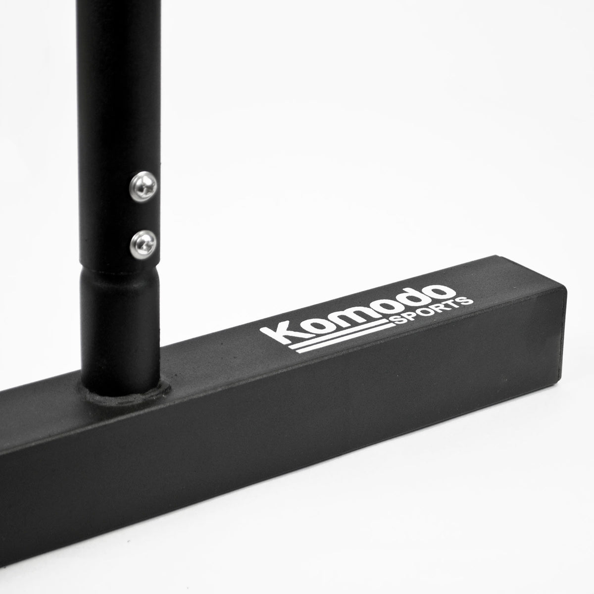 Close-up of a black metal fitness bar with a rectangular base featuring the white printed logo 'Komodo Sports'.