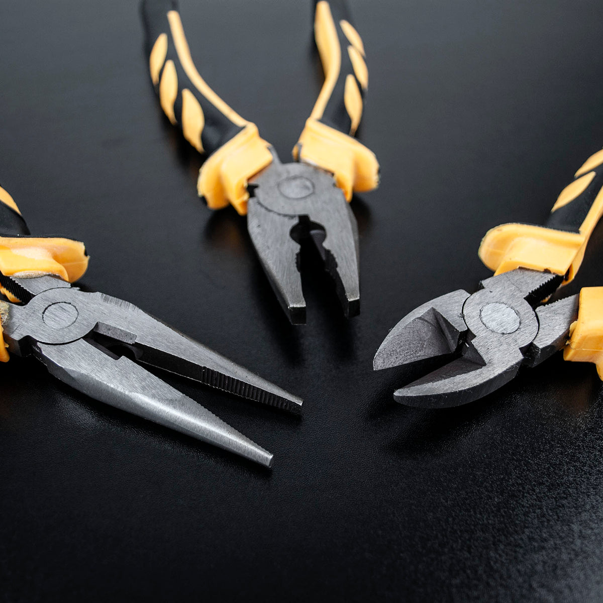 Three metal pliers with yellow and black handles arranged on a dark black background.