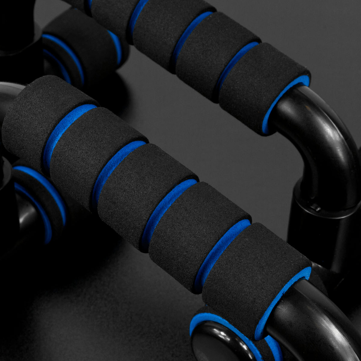 Close-up of black foam handles with bright blue trim on a dark exercise bar, photographed against a dark studio background.