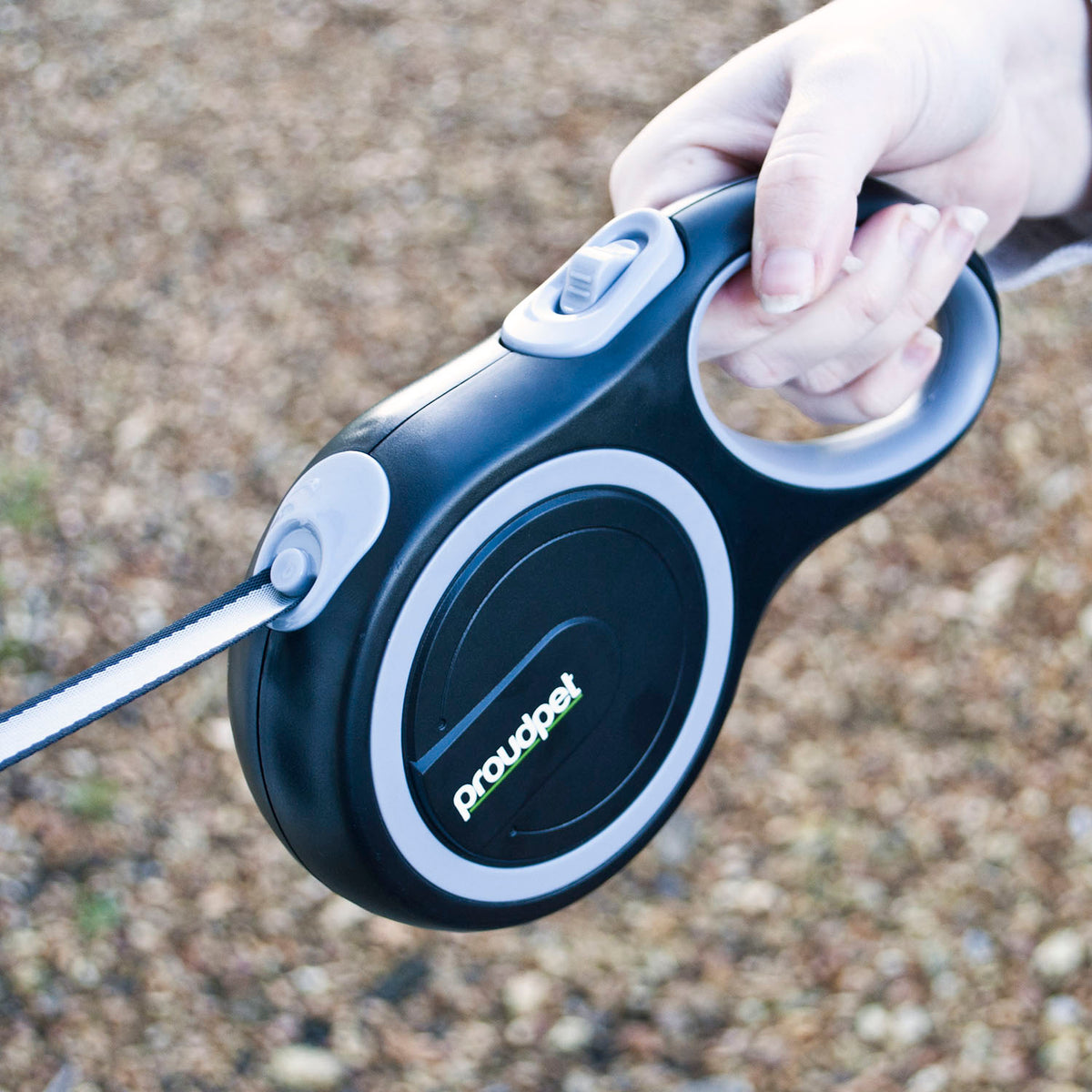 Person holding a retractable dog leash with 'Proudpet' branding against a blurred ground background