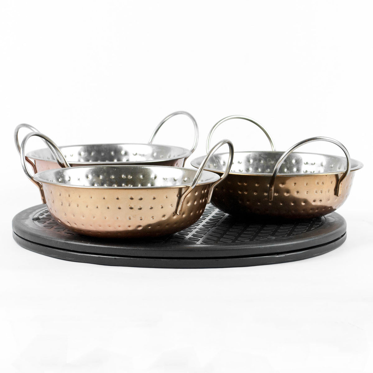 Three copper dishes with double loop handles, arranged on a round black lazy susan against a white background.