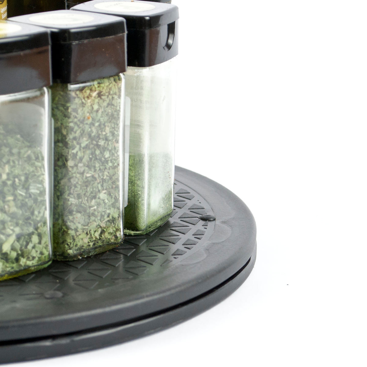 Close-up of a black circular spice rack holding three clear glass jars with black lids, filled with dried herbs and spices, on a white background.