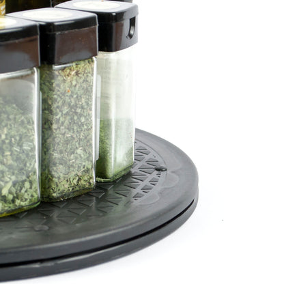 Close-up of a black circular spice rack holding three clear glass jars with black lids, filled with dried herbs and spices, on a white background.