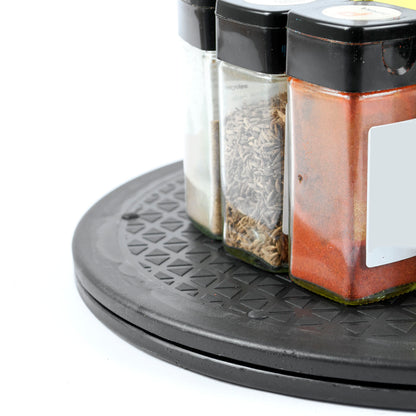 A close-up of a black plastic spice rack holding three clear glass spice jars with black lids, filled with white, brown, and reddish-brown spices, on a white background.