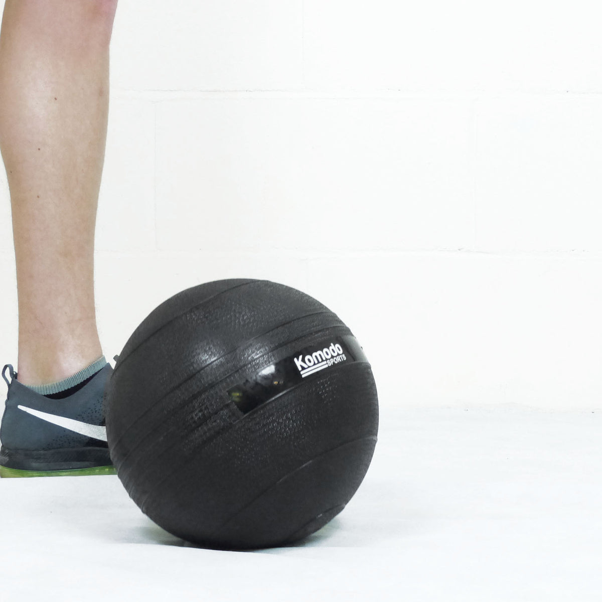 A black Komodo slam ball on a white floor next to a person's leg and shoe.
