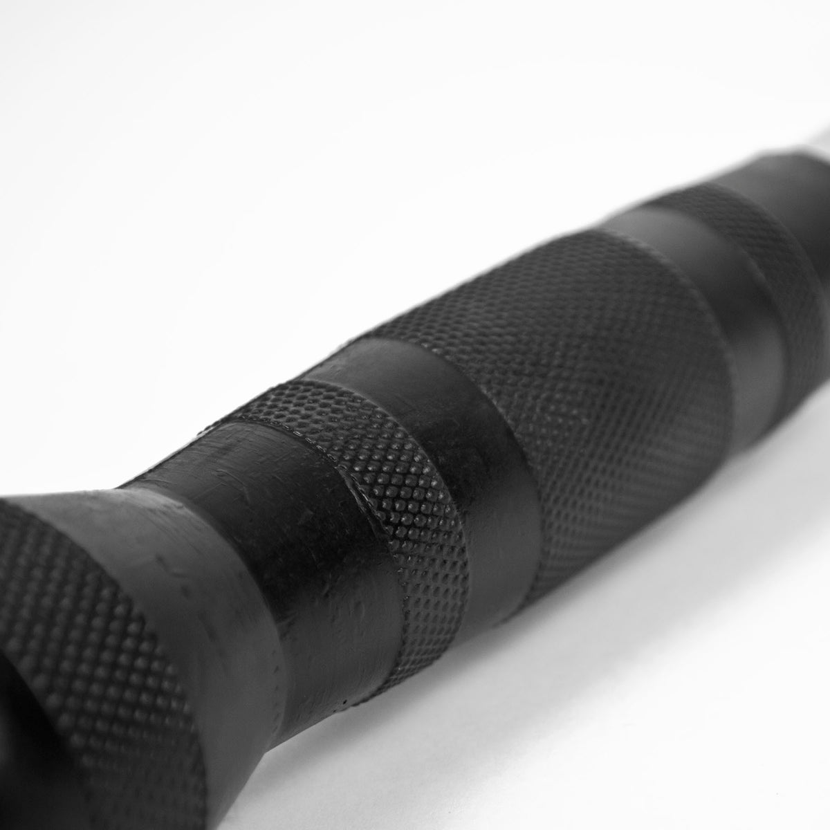 Close-up of a black textured cylindrical handle or grip with knurled and ribbed sections, photographed on a plain white background.
