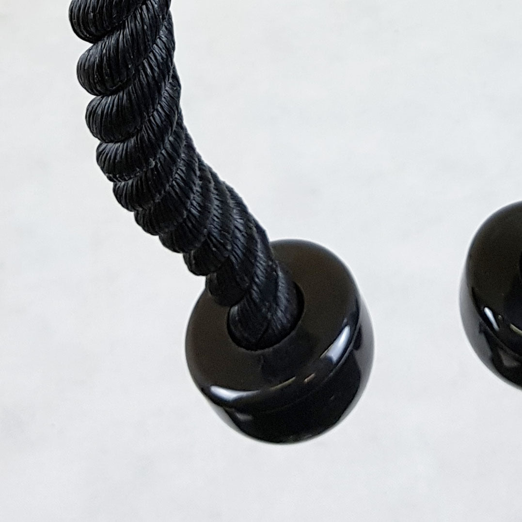 Close-up of a black twisted rope threaded through a glossy black circular ring or bead, photographed against a plain light background.