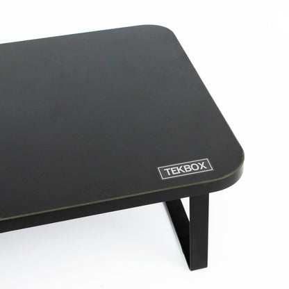 A close-up of a black rectangular tabletop with rounded corners and a visible TEKBOX logo badge on the front edge, set against a plain white background.