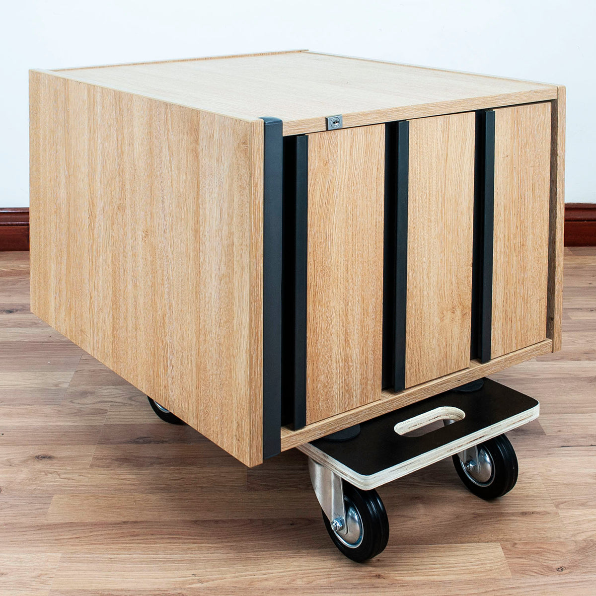 A wooden storage cabinet on a wheeled dolly cart, featuring a light oak wood grain finish with black vertical handle accents and black caster wheels.