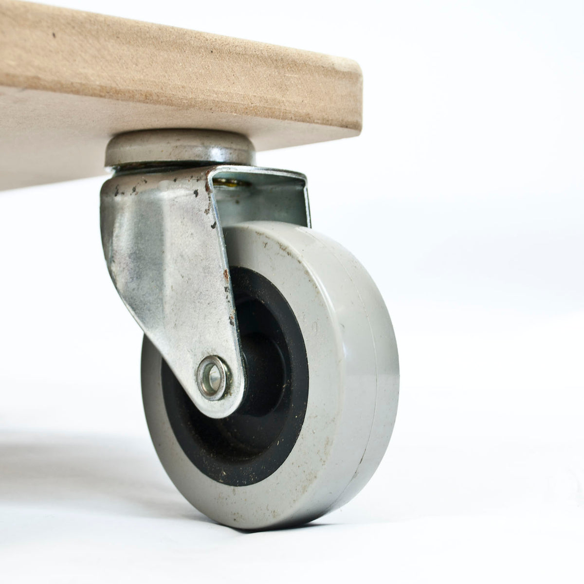 Close-up of a gray industrial caster wheel with a metal swivel bracket and a light wood board attached above it, photographed on a white background.