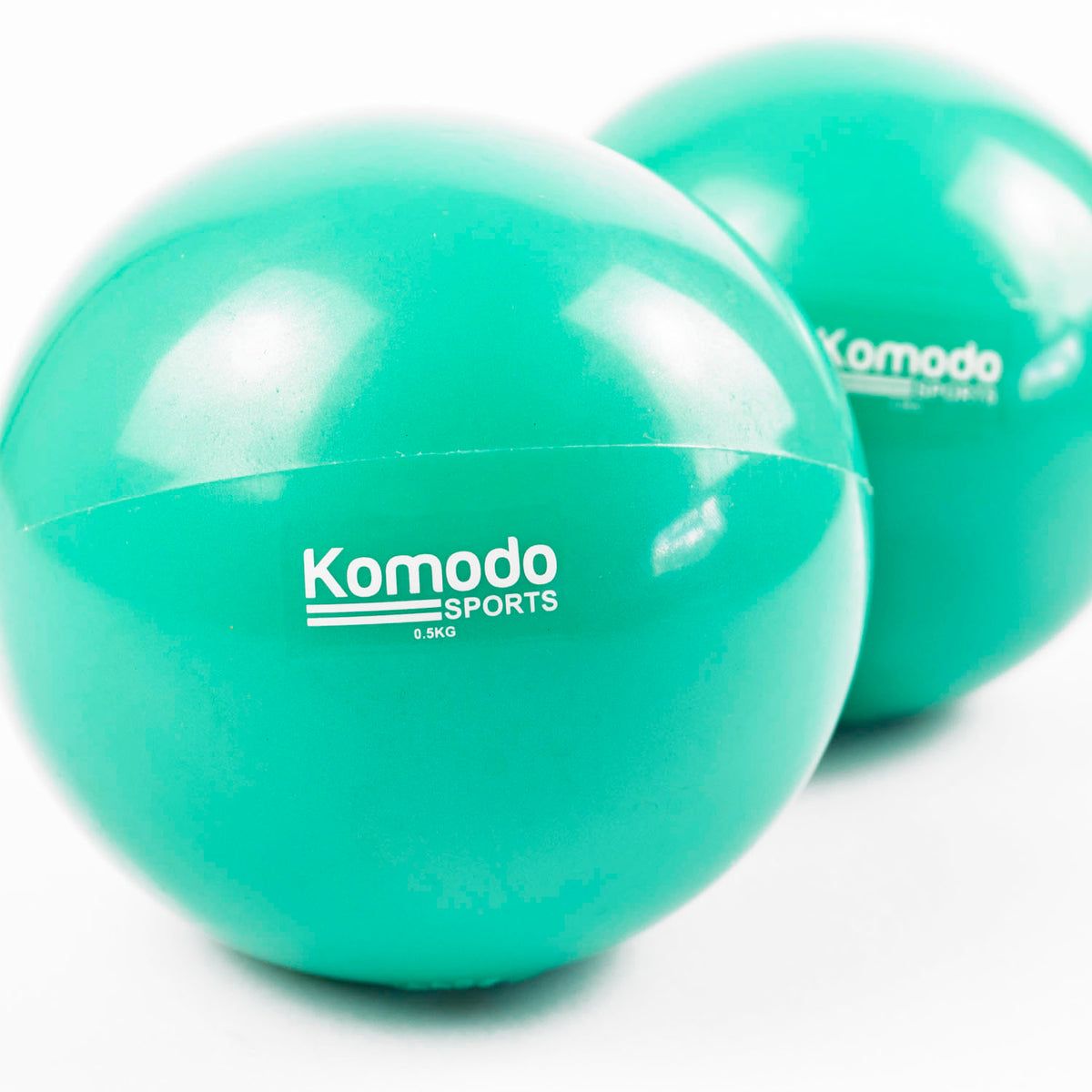 Two green Komodo Sports exercise balls on a clean white background, with one ball in sharp focus in the foreground and the second ball softly blurred in the background.