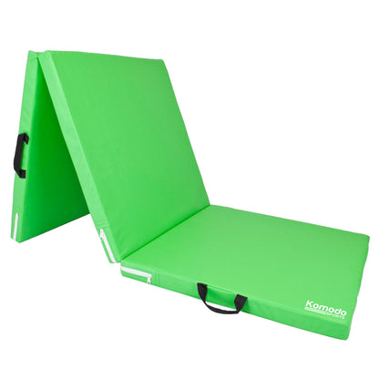A bright green portable yoga mat folded into a chair position, featuring black carrying handles and a white Komodo brand logo on the bottom right corner.