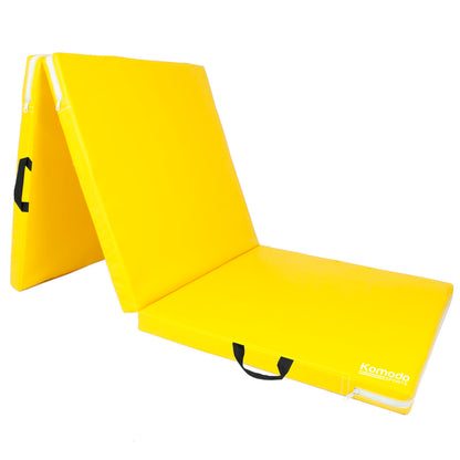 A bright yellow foldable pilates mat shown partially unfolded on a clean white background. The mat features black carrying handles and a white 'Komodo' brand logo on the bottom right corner.
